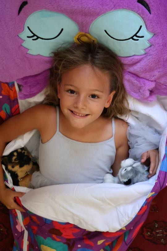 Young girl enjoying the Unicorn Pink Sleeping Bag at a sleepover, cozy and smiling inside the bag.
